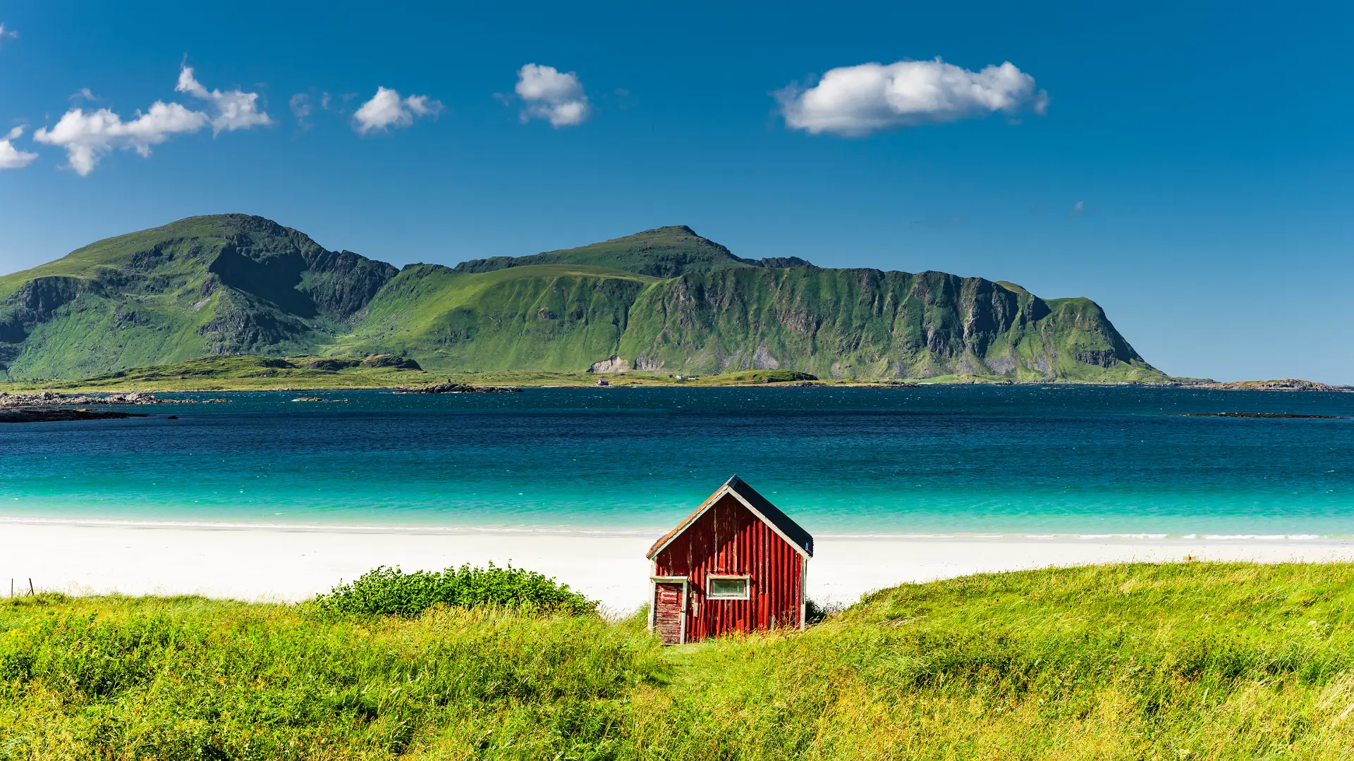 Coastal beach walk in the Lofoten Islands, Norway, with white sand, turquoise water, and mountains rising behind the shoreline.
