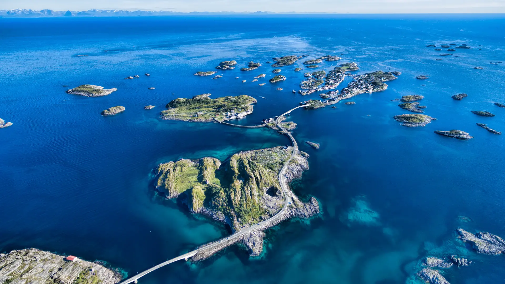 Aerial view of coastal roads and bridges connecting islands in the Lofoten Islands, Norway, surrounded by clear blue water.
