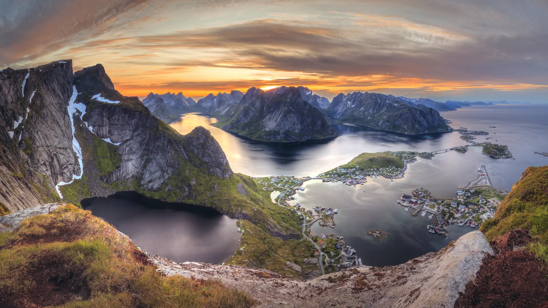 Mountain peaks, fjords, and a coastal village in the Lofoten Islands, Norway, seen from a viewpoint along a hiking route.