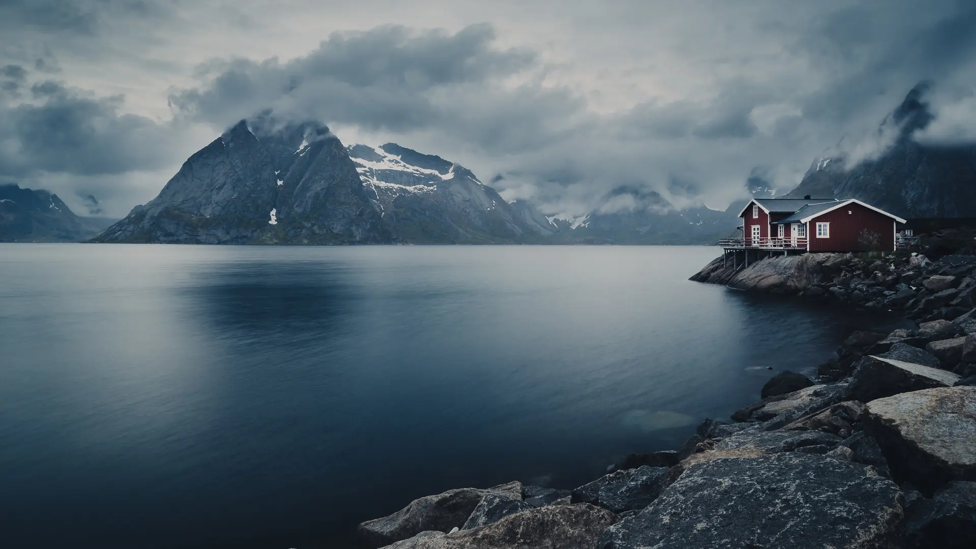 Low clouds over a fjord with mountains and a traditional rorbu in the Lofoten Islands, Norway.