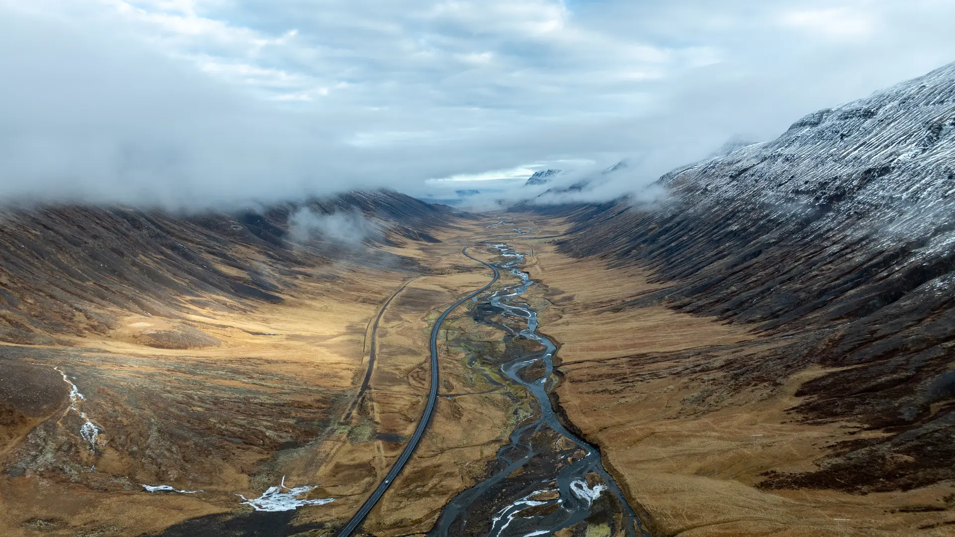 Remote valley road winding through a broad mountain landscape in Iceland.