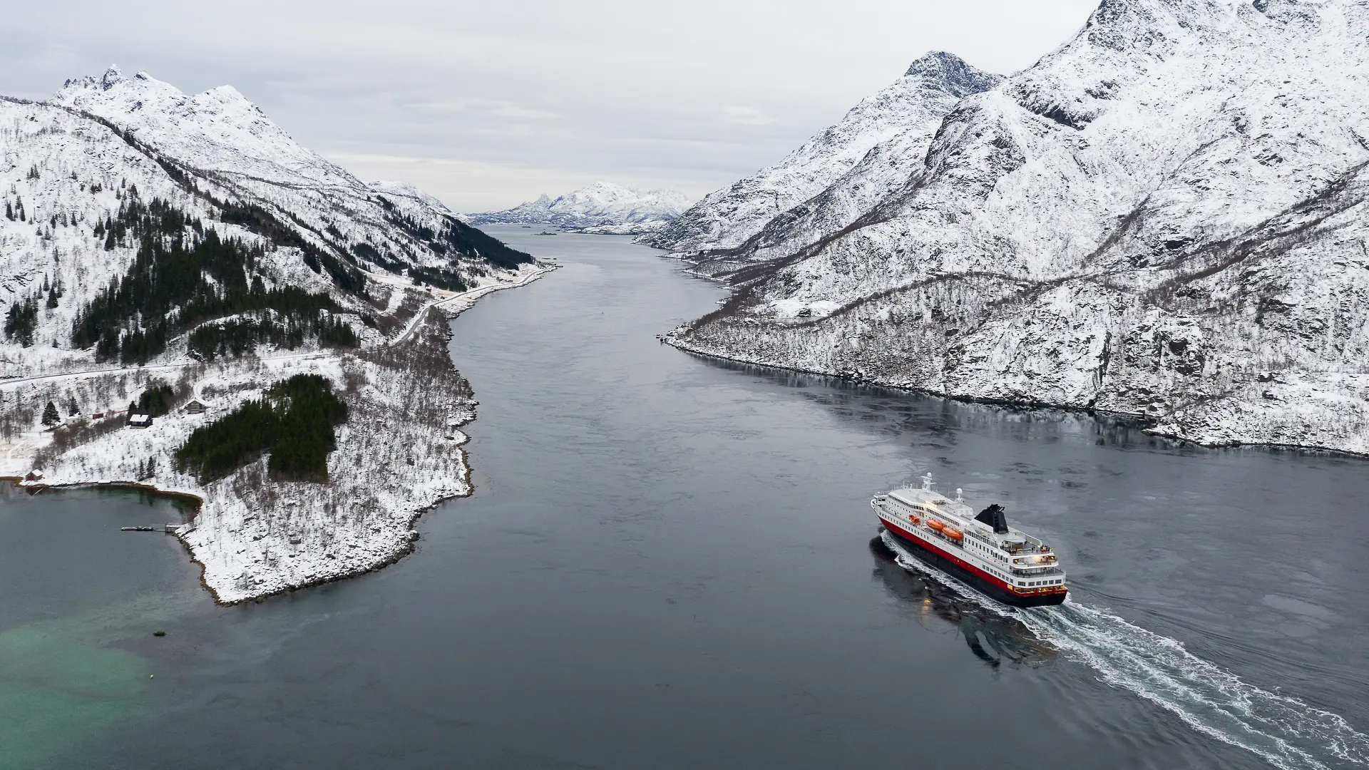 Car ferry traveling through a snow-covered fjord in the Lofoten Islands, Norway, during winter.