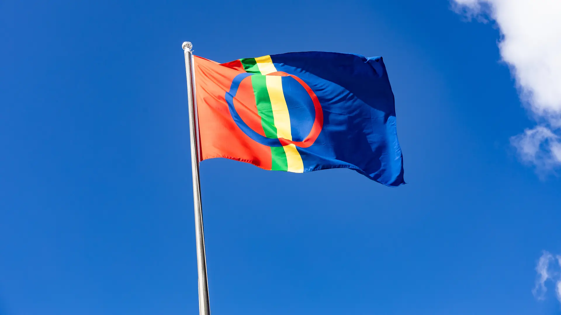 Sápmi flag flying on a flagpole against a clear blue sky.